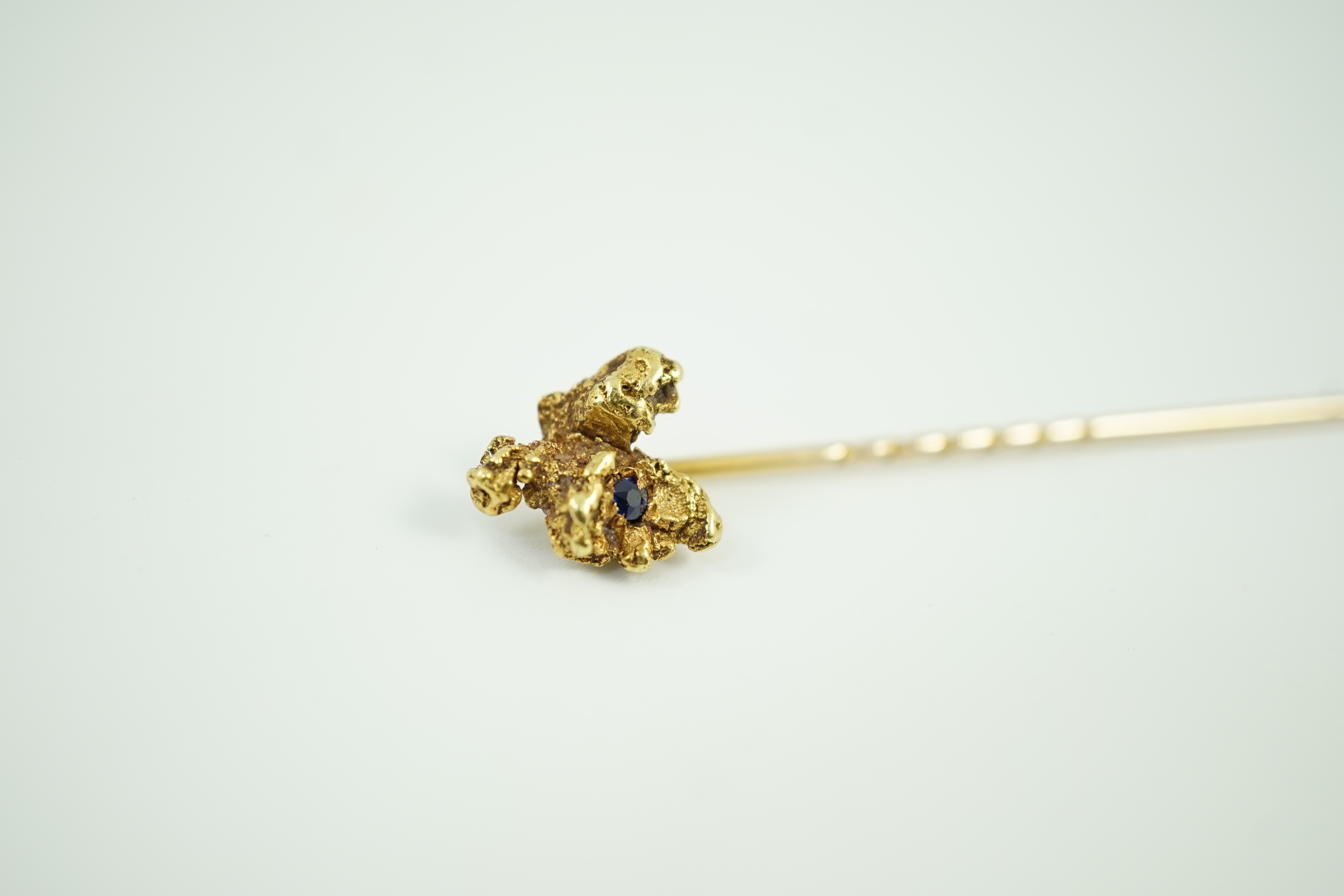 A late Victorian yellow metal and single stone sapphire set 'nugget' stick pin, 62mm, gross weight 3.2 grams.